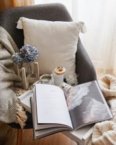 Cozy looking chair with pillow and blanket.