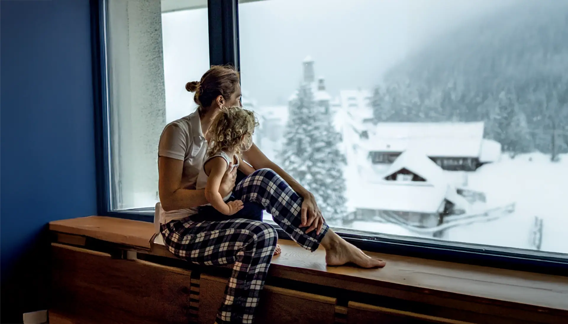 Woman sitting at a window looking out into a winter setting with a child on her lap