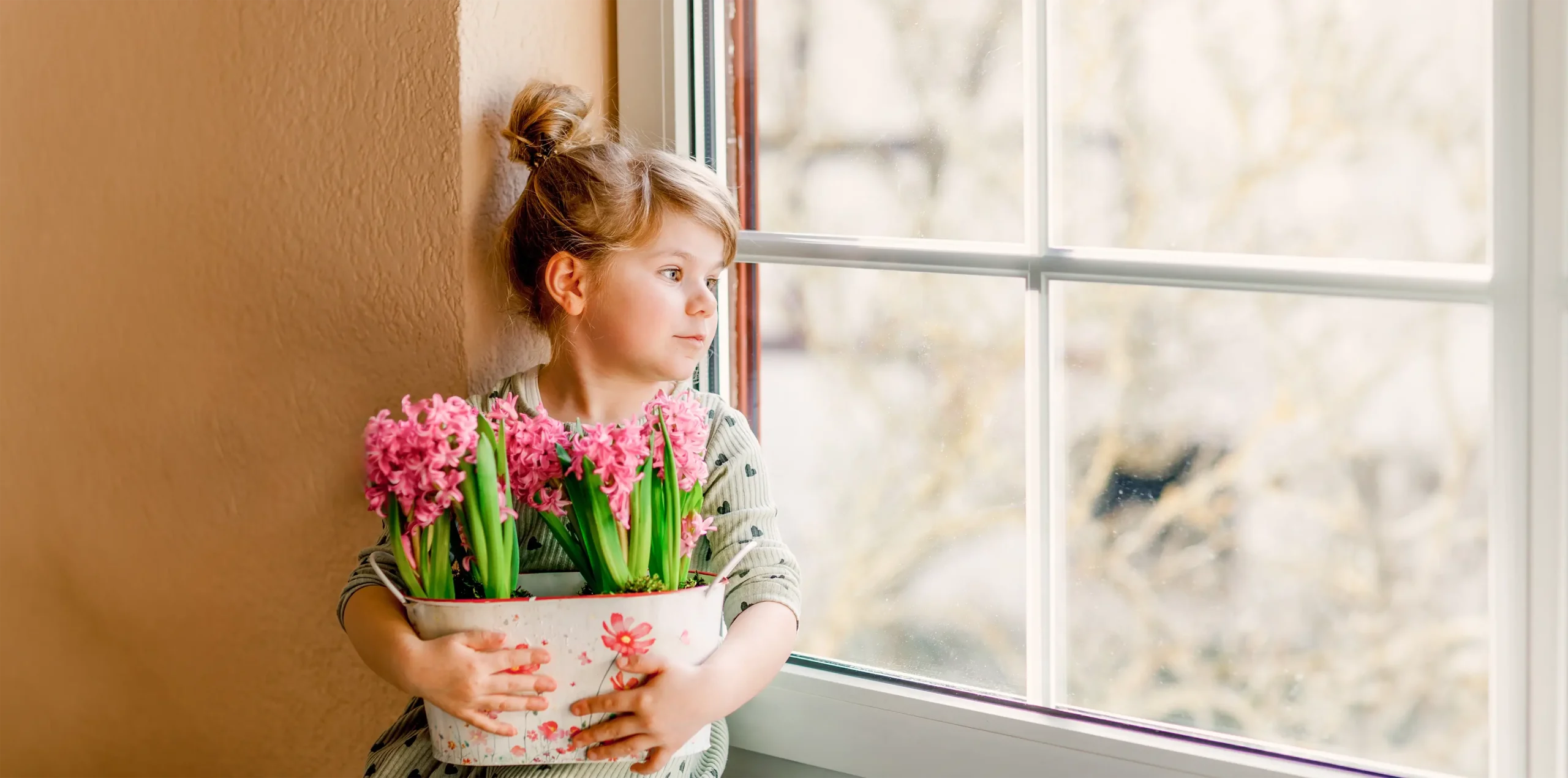 Girl sitting looking out of a window with flowers in her hand